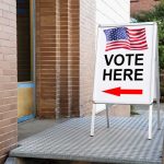 "Vote Here" sign with arrow and American flag.