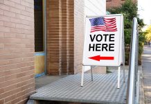 "Vote Here" sign with arrow and American flag.