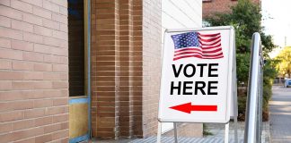 "Vote Here" sign with arrow and American flag.