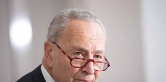 Man in suit wearing red glasses, looking serious.