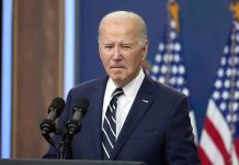 Man in suit speaking at podium with American flags.