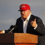 Person speaking at a podium wearing a red hat.