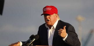 Person speaking at a podium wearing a red hat.