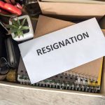 Envelope labeled "RESIGNATION" atop office supplies in box.