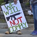 Protest sign reads: "We Will Not Comply".