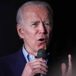 Man speaking into a microphone, black background.