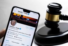 Smartphone displaying Twitter profile beside a judge’s gavel.