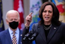 Woman speaking at podium, man with mask behind.