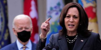 Woman speaking at podium, man with mask behind.