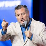 Man speaking into microphone, gesturing with hand.