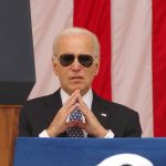 Man in sunglasses in front of American flag.