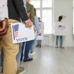 People standing in line holding voting papers.