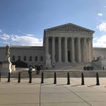 U.S. Supreme Court Building with flag and people outside.