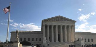 U.S. Supreme Court Building with flag and people outside.