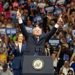 Man and woman celebrating on stage with supporters.