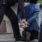 Police officers arresting and handcuffing a man kneeling.