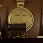 Judge's chair, gavel, flags, and scales of justice emblem.