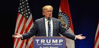 Man speaking at podium with American flags behind.