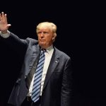 Man in a suit waving against dark background.