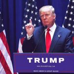 Man speaking at podium with American flags behind.