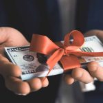 Hands holding stack of hundred-dollar bills with ribbon.