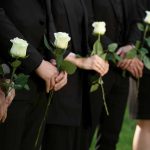 People in black holding white roses in a line.