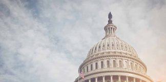 Capitol dome with American flag, under cloudy sky.