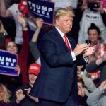 Man clapping at a rally with audience cheering.