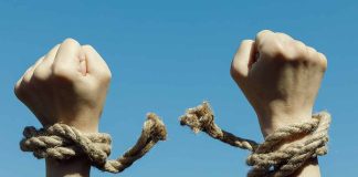 Hands with broken rope against blue sky