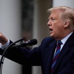 Man speaking at podium outdoors gesturing with hand