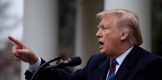 Man speaking at podium outdoors gesturing with hand