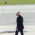 Person walking on tarmac wearing a black mask.