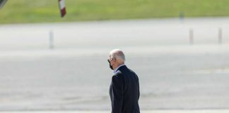 Person walking on tarmac wearing a black mask.