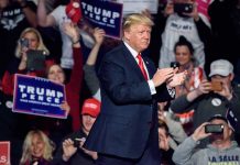 Man clapping at a rally with audience cheering.