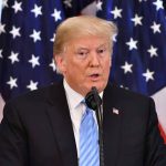 Man speaking at podium with American flags behind