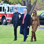 Three people walking on grass near fire truck.