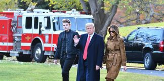 Three people walking on grass near fire truck.