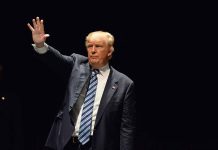 Man in a suit waving against dark background.