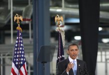 Man speaking at podium with flags behind him.