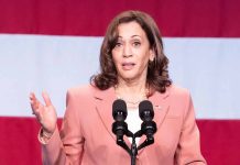 Woman speaks at podium with red and white background.