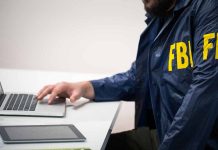 Person in FBI jacket using laptop at desk