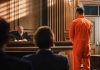 Man in orange jumpsuit stands in courtroom facing judge