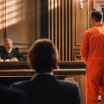 Man in orange jumpsuit stands in courtroom facing judge