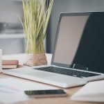 Laptop on desk with plant and coffee mug.
