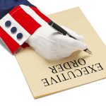 Gloved hand writing on paper labeled executive order