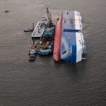 Capsized ship with cranes and tugboats around it