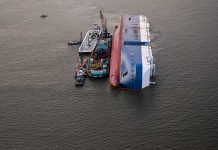 Capsized ship with cranes and tugboats around it