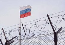 Barbed wire fence with Russian flag in background