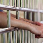 Hands resting on prison bars