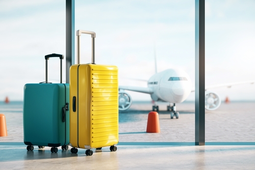 travel_2479523943 featured image Two suitcases at airport window with airplane outside